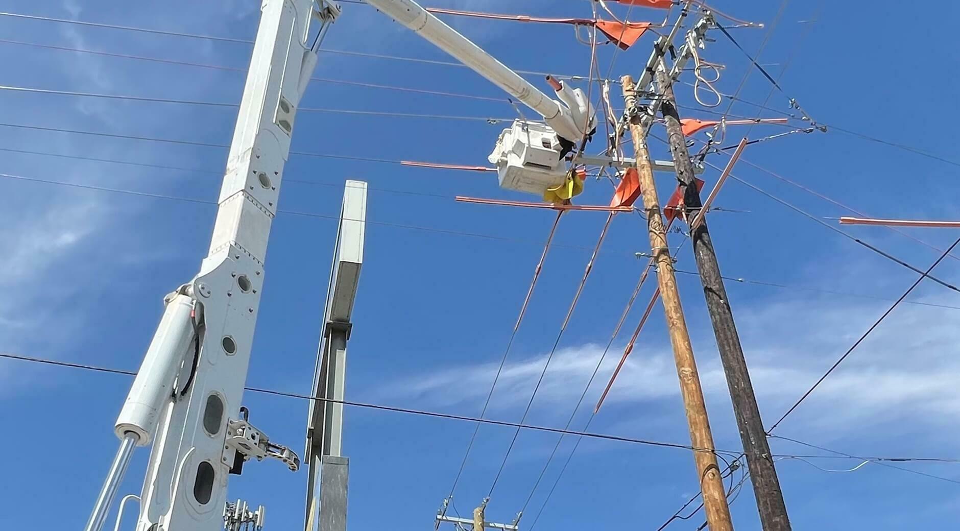 Utility worker in a bucket truck repairing power lines while wearing safety gear and an orange vest.
